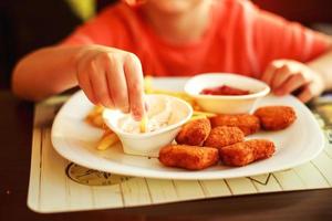 ragazzo mangiare veloce cibo nel un' bar. il bambino mangiare francese patatine fritte con pepite foto