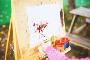 poco ragazza disegna su il cavalletto. il bambino vernici foto