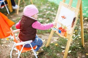 poco ragazza disegna su il cavalletto. il bambino vernici foto