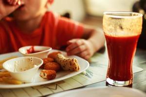 ragazzo mangiare veloce cibo nel un' bar. il bambino mangiare francese patatine fritte con pepite foto