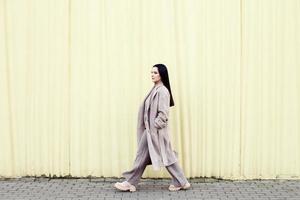 donna a piedi nel un' beige cappotto contro urbano città sfondo. foto