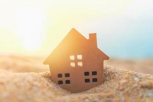 primo piano del piccolo modello di casa sulla sabbia con sfondo di luce solare foto
