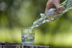 mano versando acqua potabile dalla bottiglia in vetro con sfondo naturale foto