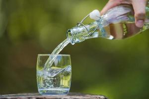 mano versando acqua potabile dalla bottiglia in vetro con sfondo naturale foto