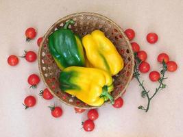peperoni in un cesto di vimini accanto ai pomodori su uno sfondo di tavolo beige