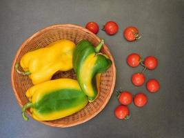 peperoni in un cesto di vimini accanto ai pomodori su uno sfondo di tavolo scuro foto