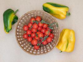 pomodori in un cesto di vimini accanto a peperoni su uno sfondo di tavolo beige