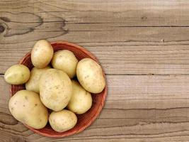 patate in un cesto di vimini su uno sfondo di tavolo in legno foto