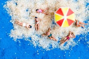 persone in miniatura che prendono il sole sulla spiaggia, concetto di estate foto