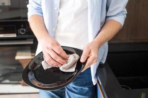 un' uomo nel un' camicia salviette piatti con un' asciugamano in piedi nel il cucina. il uomo nel il cucina foto