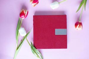 un' rosso pelle libro con un sbalzato posto per testo, bugie su un' viola sfondo Il prossimo per fiori e tulipani foto