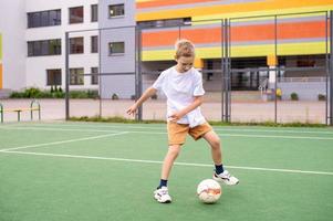 un' adolescenziale ragazzo sta su un' verde campo nel il scuola cortile con un' calcio palla nel formazione foto