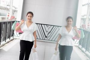ritratto di contento sorridente donna con shopping borse nel corridoio camminare modo. bellissimo donna con un' carta Borsa. foto