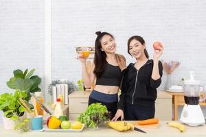 asiatico attivo Due donne fratello nel abbigliamento sportivo godere mangiare frutta salutare Alimenti. bellissimo ragazza, sorella Tenere un' bicchiere di arancia succo e mele nel il cucina foto