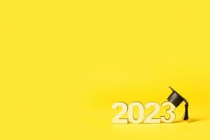 classe di 2023 concetto. di legno numero 2023 con laureato berretto su podio su giallo sfondo con copia spazio foto