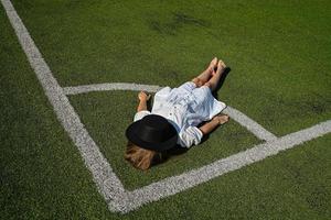 un' ragazza è dire bugie su un' calcio campo nel un' bianca vestire. sfondo per il progettista. foto