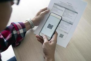 un' uomo usi un' smartphone per scansione il qr codice per pagare mensile credito carta fatture dopo ricevente un fattura inviato per casa. in linea conto pagamento concetto foto