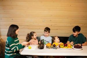 madre con quattro bambini mangiare frutta nel di legno nazione Casa su fine settimana. foto