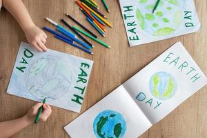un' bambino a casa a il tavolo disegna il pianeta terra con un' mondo carta geografica con multicolore matite e pennarello penne su bianca carta. pace e terra giorno concetto. foto
