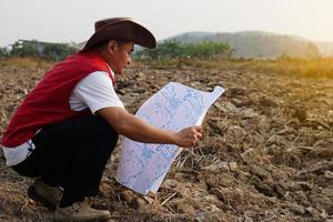 asiatico uomo esploratore indossa cappello, rosso veste camicia, detiene carta geografica per Esplorare terra confine. concetto, terra pianificazione, esplorando proprietà. geodetico sondaggio la zona. Tesoro a caccia su terra. foto