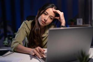 asiatico attività commerciale donna fa col tempo Lavorando a partire dal casa nel vivente camera a in ritardo notte dovuto per covid19 pandemia. ragazza avere lotto di lavori e problema su computer il computer portatile. foto