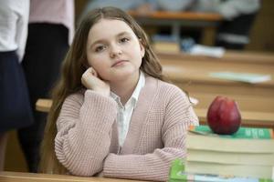 ragazza scolara a il scrivania. ragazza nel il aula con libri e un Mela. secondario scuola. indietro per scuola. foto