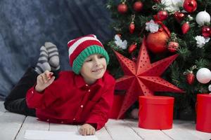 poco ragazzo scrive un' lettera per Santa claus, pensa di i regali per Natale. foto