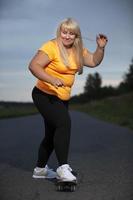 paffuto di mezza età europeo donna, sovrappeso, nel un' tuta, impara per cavalcata un' skateboard, va nel per gli sport. foto