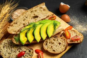 affettato avocado con aneto le foglie su baguette pane su nero sfondo, salutare cibo foto