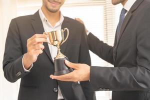 bene lavoro di risultato, contento successo asiatico giovane uomo d'affari, uomo dipendente Tenere d'oro trofeo tazza, squadra ottenere premiato per vincente a partire dal caucasico uomo capo. celebrazione di lavoro di squadra di attività commerciale. foto