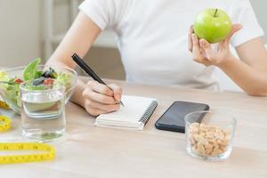 dieta, dieta attraente asiatico giovane donna, ragazza Lavorando, Scrivi dieta Piano giusto nutrizione con mangiare fresco verdure insalata è cibo per bene Salute. dietologo per peso perdita di salutare a casa. foto