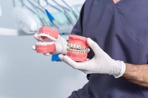 Ritaglia anonimo stomatologo con dentiere seduta nel clinica foto