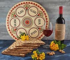 Pesach celebrazione concetto - ebraico vacanza pesach. sfondo con giallo fiori con bicchiere di vino, matzah e piatto di seder su blu sfondo. tradizionale ebraico iscrizioni su piatto. foto