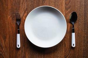 piatto bianco con un cucchiaio e una forchetta su un tavolo di legno foto