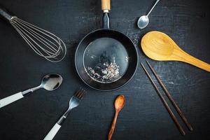 utensili da cucina e una padella nera sul fondo della tavola nera foto