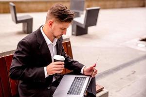 giovane tipo nel un' completo da uomo lavori su un' computer nel il parco di un' attività commerciale centro caffè nel il suo mani foto