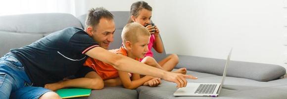 immagine di sorridente persone padre 30s con figlio e figlia abbracciare insieme su divano a casa e utilizzando argento il computer portatile foto