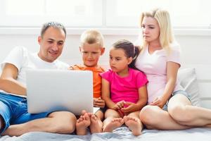 amorevole famiglia guardare a un' il computer portatile dire bugie giù su letto a casa foto