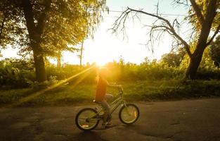 poco ragazza con equitazione bicicletta a tramonto foto