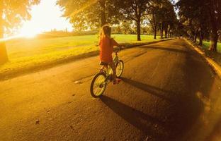 poco ragazza con equitazione bicicletta a tramonto foto