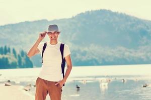 bello uomo al di sopra di verde natura e blu lago in piedi . avventura, viaggiare, turismo e tempo libero concetto - giovane ragazzo rilassante foto