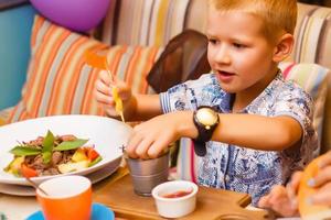 carino prescolastico ragazzo ragazzo mangia pranzo nel bar o ristorante, estate foto