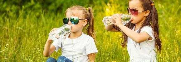 piccolo bambini rinfrescante loro stessi con acqua nel il parco. poco ragazza potabile acqua modulo un' bottiglia nel il città. foto