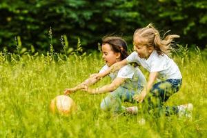 Due piccolo contento ragazze giocando con palla all'aperto, in esecuzione insieme nel estate parco foto