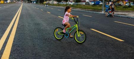 bambini apprendimento per guidare un' bicicletta su un' viale fuori. poco ragazze equitazione Bici su asfalto strada nel il città indossare caschi come protettivo Ingranaggio. foto