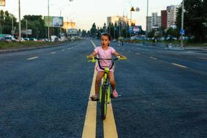 poco brunetta ragazza equitazione bicicletta su strada a tramonto foto