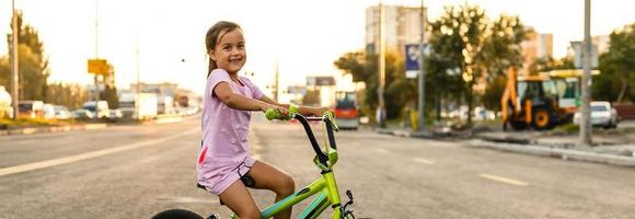 bambini apprendimento per guidare un' bicicletta su un' viale fuori. poco ragazze equitazione Bici su asfalto strada nel il città indossare caschi come protettivo Ingranaggio. foto