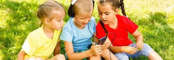 tre bambini nel il parco siamo seduta su il erba con un' Telefono foto