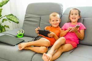 fratello e sorella seduta su divano a casa utilizzando mobile Telefono. vicino su sorpreso figlia e frustrato figlio guardare a dispositivo schermo. tecnologia nuovo generazione dipendente con gadget concetto foto