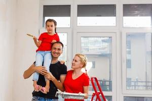 il giovane gioioso famiglia fa riparazione a casa, essi dipingere il parete con Aiuto di piastre foto